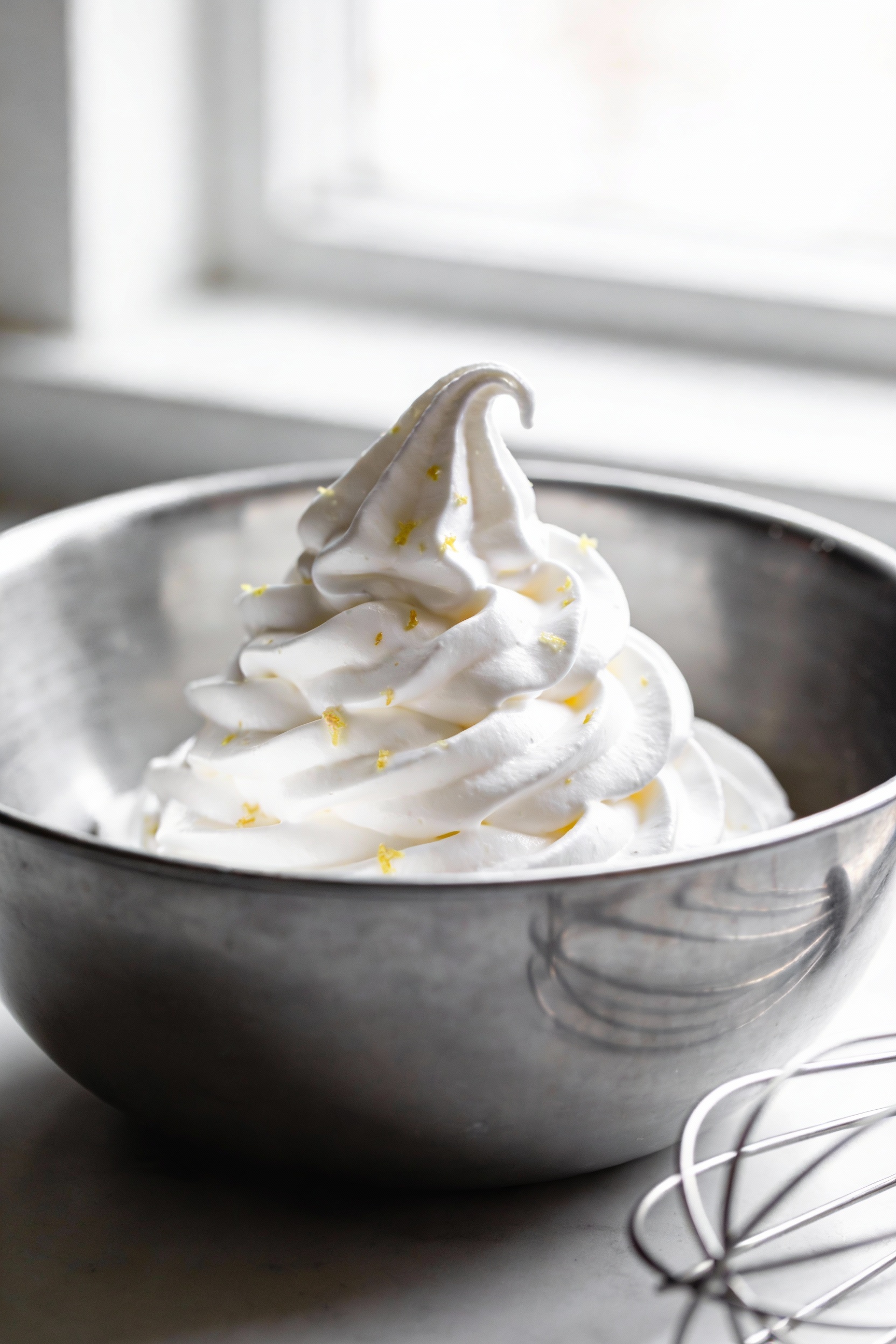 Cooking process: glossy stiff-peaked meringue in a spotless stainless-steel mixing bowl, smooth shiny peaks holding shap
