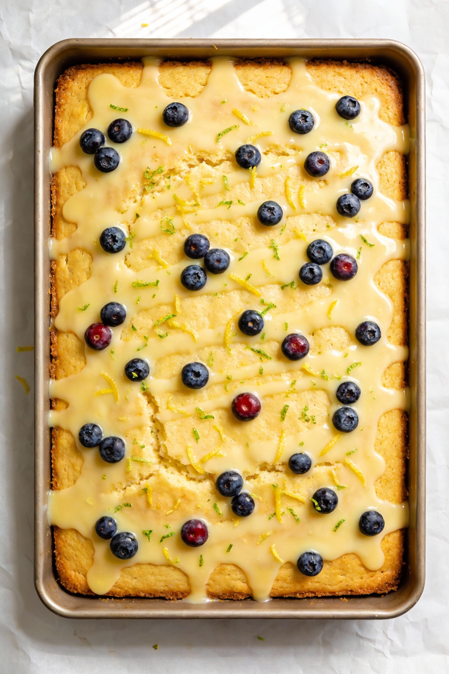 Overhead shot of a finished lemon blueberry sheet cake made from boxed lemon mix, glossy lemon glaze dripping over the s