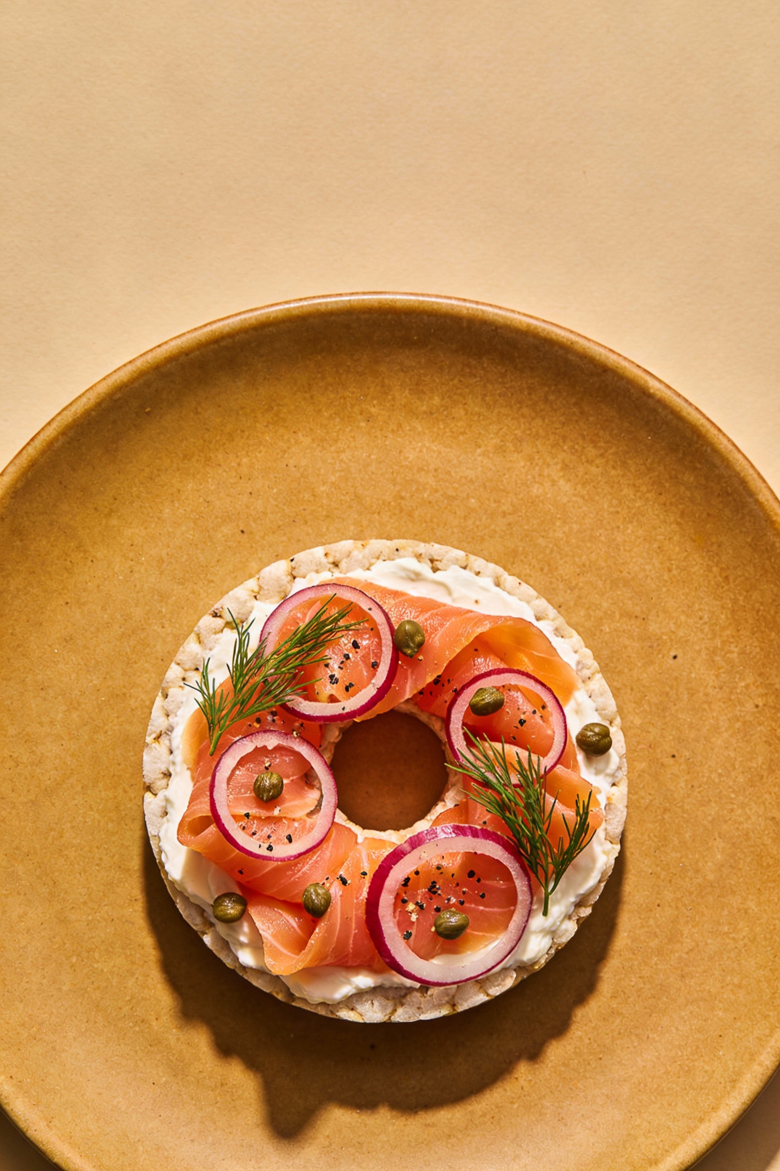Overhead shot of a smoked salmon “bagel” rice cake: cream cheese layer, folded smoked salmon ribbons, thin red onion rin