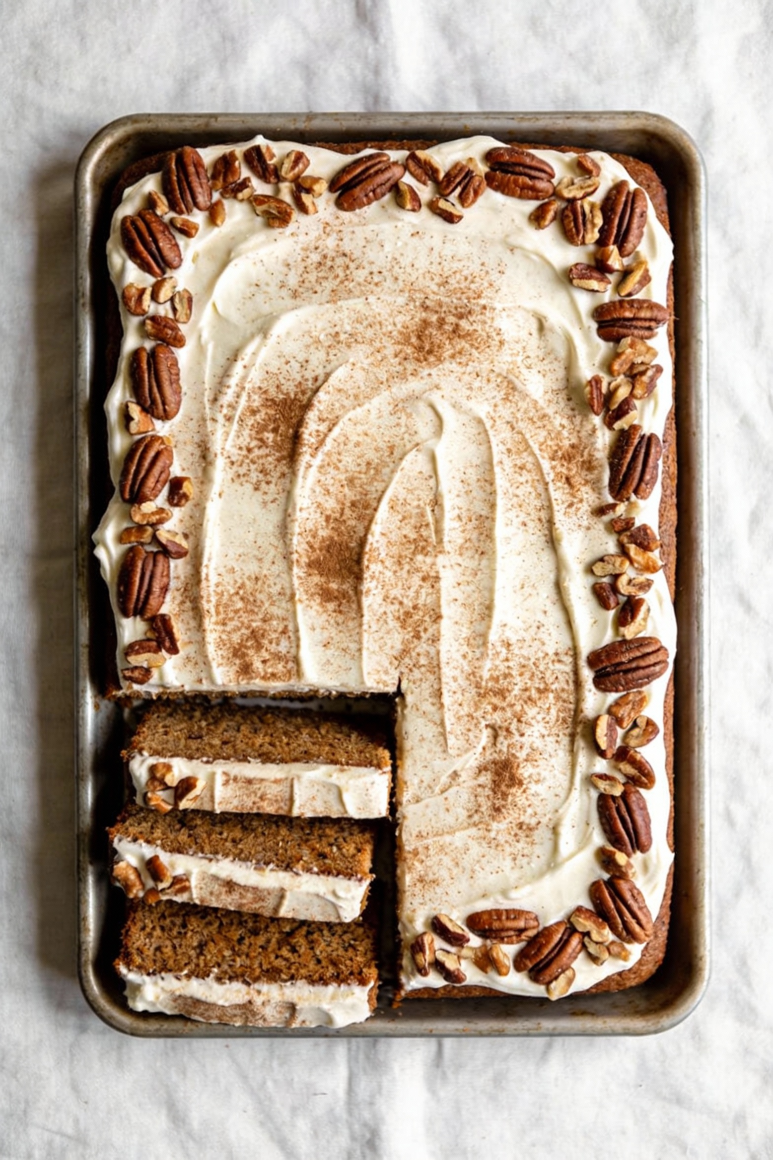 Overhead shot of a frosted 9x13 spice sheet cake with smooth cream cheese frosting, cinnamon dusting, and a border of ch