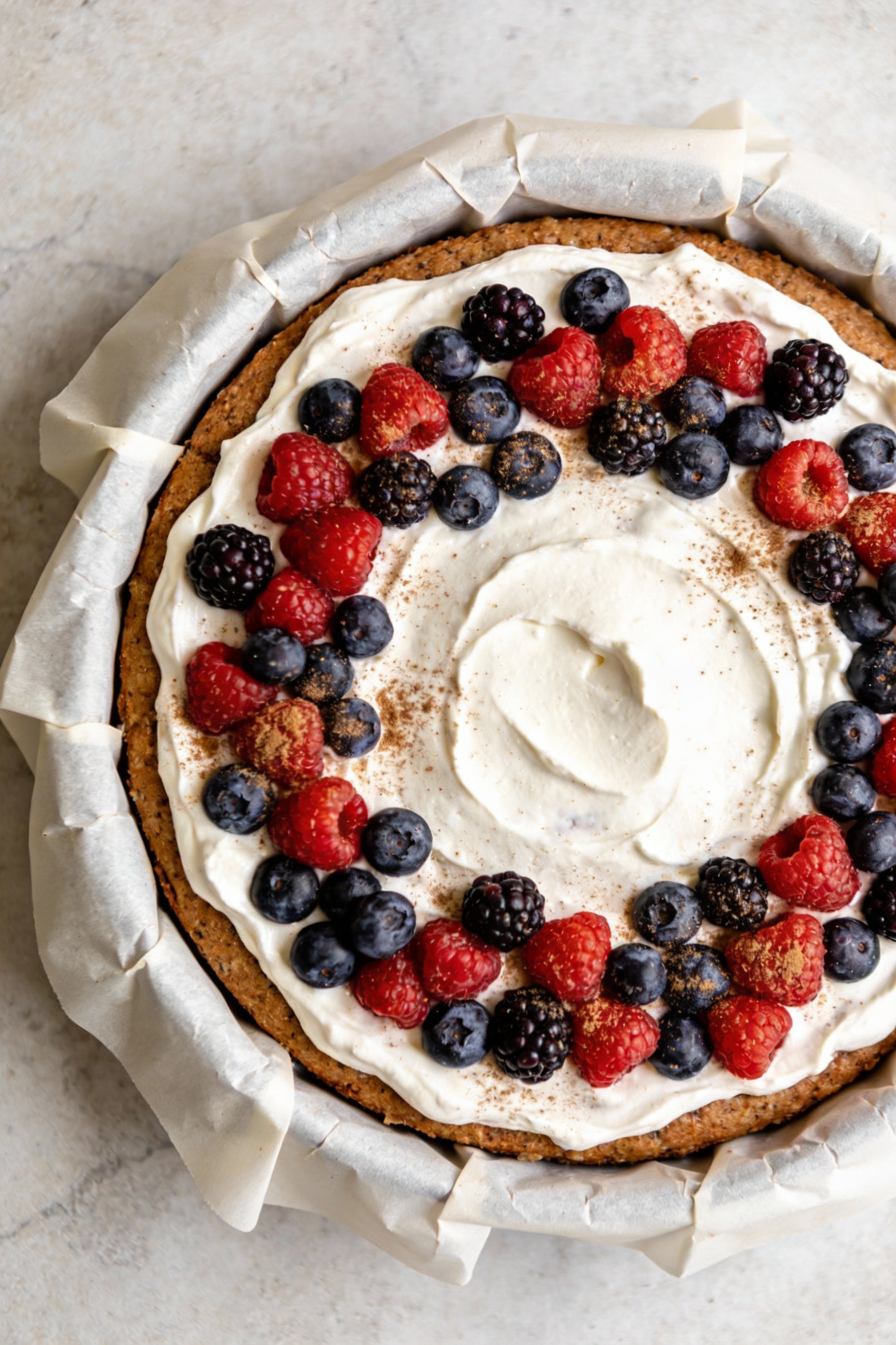 2. Overhead shot of a 9-inch round healthy cake with parchment-lined clean edges, evenly spread yogurt frosting, topped 