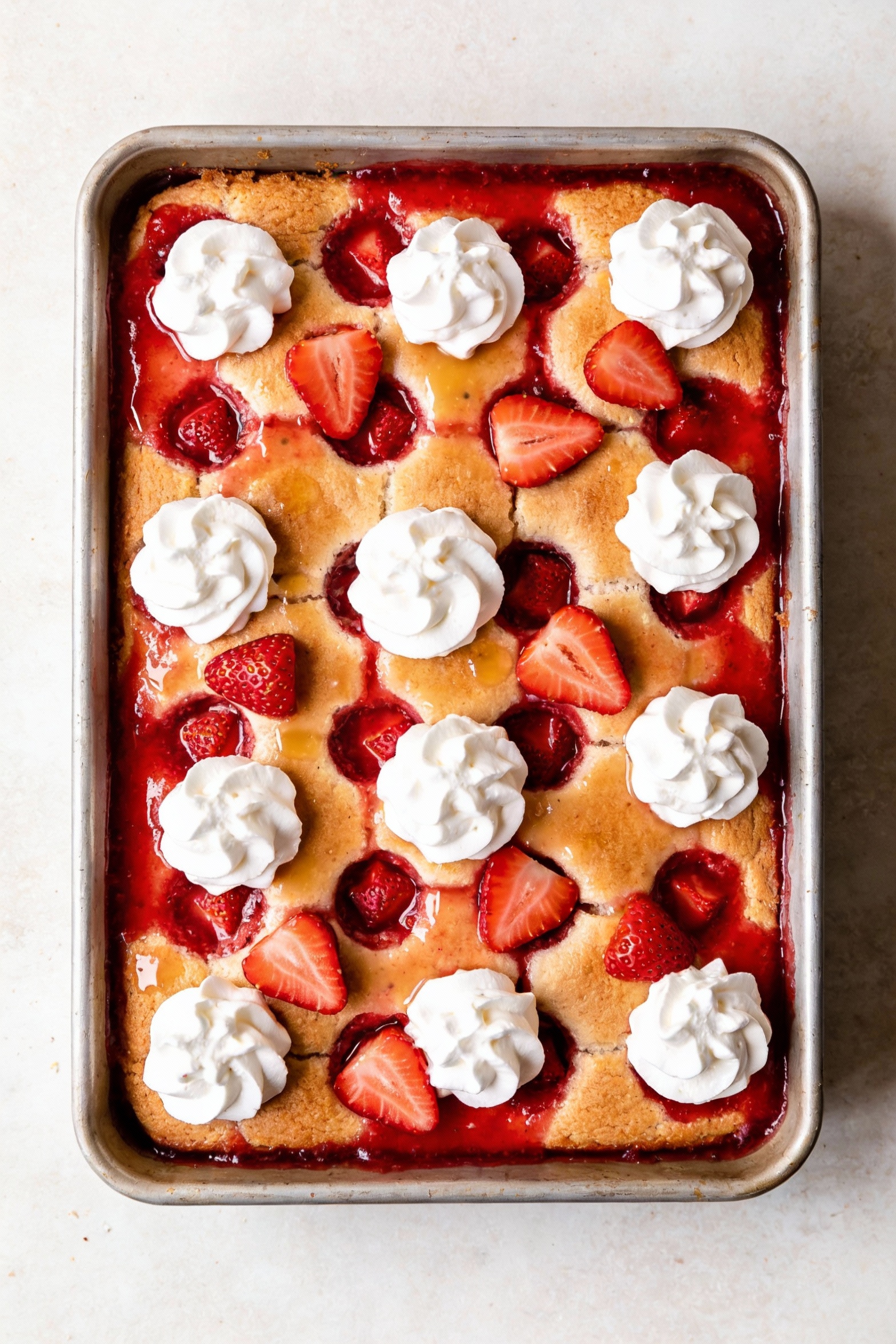 Overhead shot of strawberry poke cake in a 9x13 pan with evenly spaced poke holes and sweetened condensed milk-strawberr