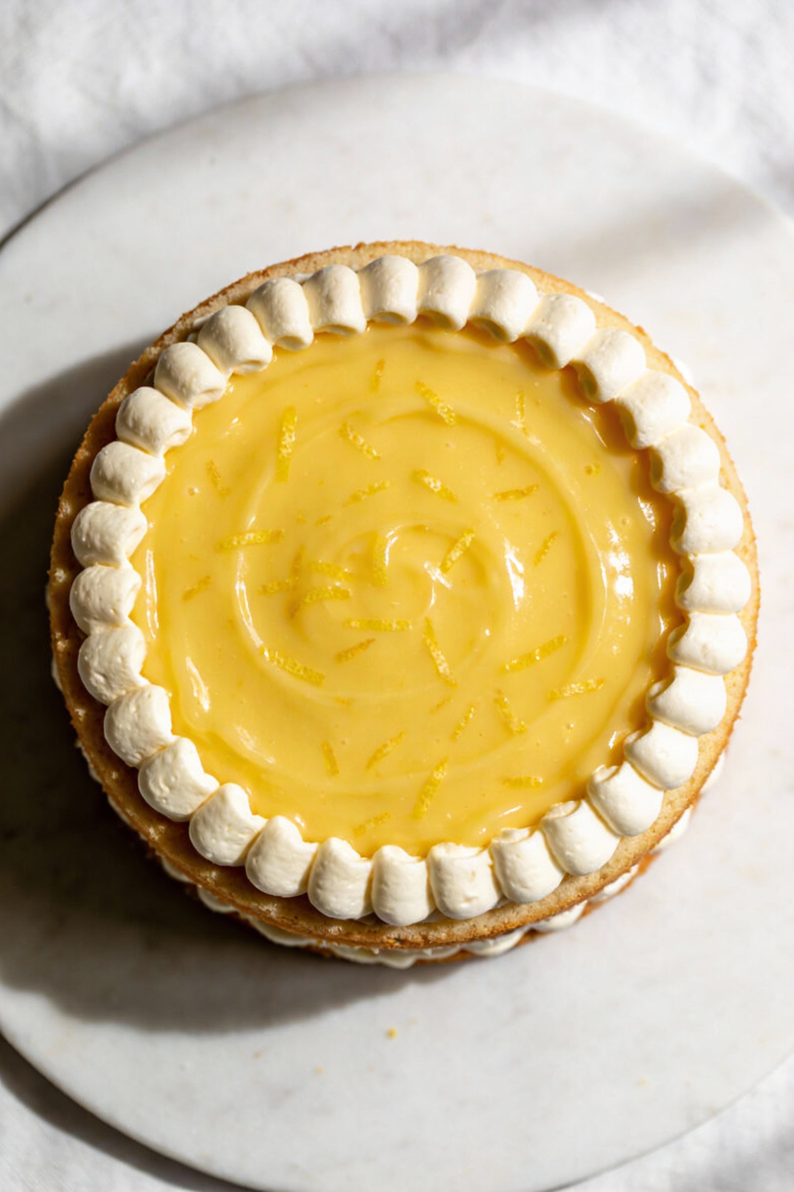 Overhead shot of a frosted cake layer showing a neat buttercream “dam” ring with lemon curd spread in the center, bright