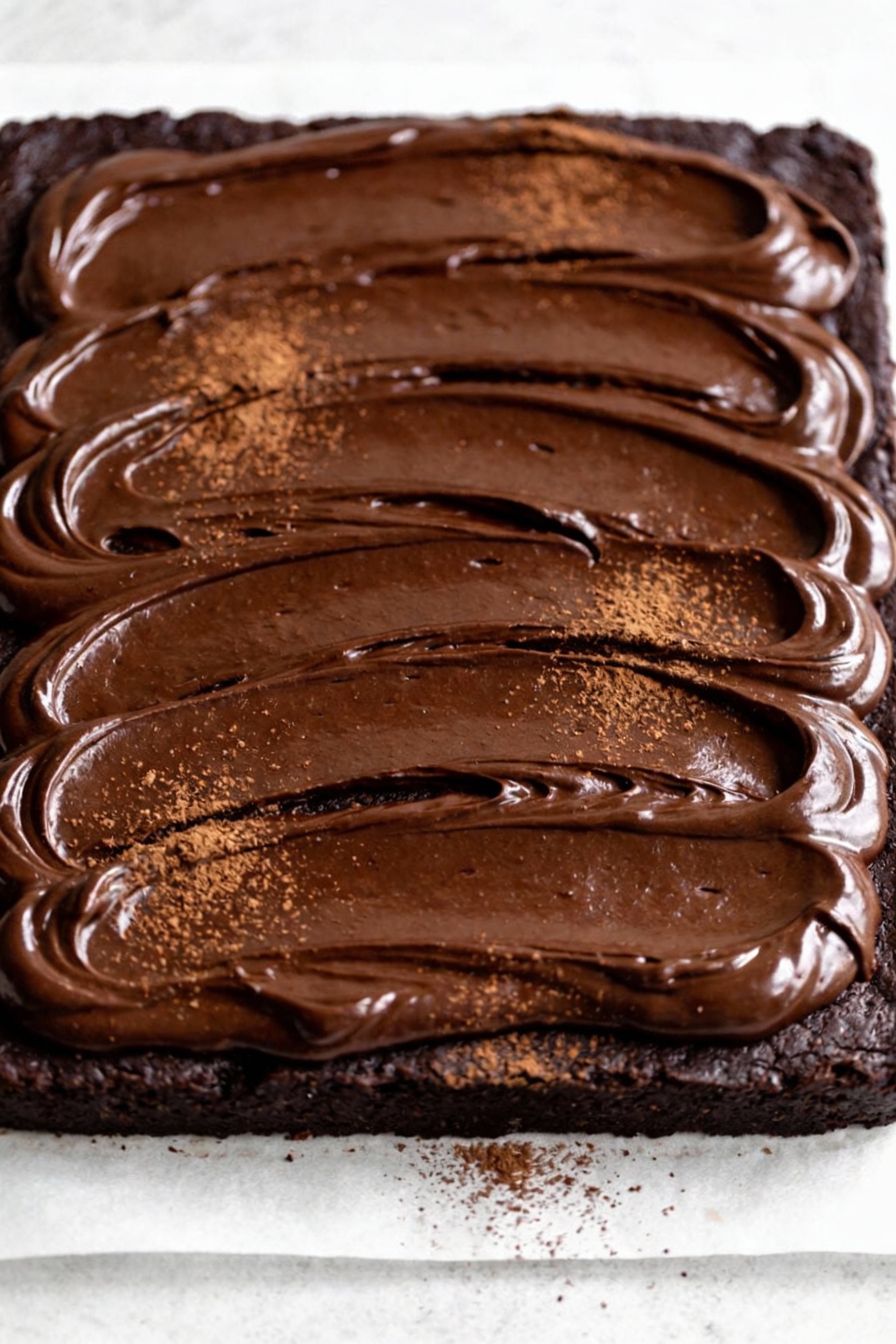 Overhead shot of a glossy deep chocolate fudge gluten-free sheet cake with smooth chocolate ganache swirls and a light s