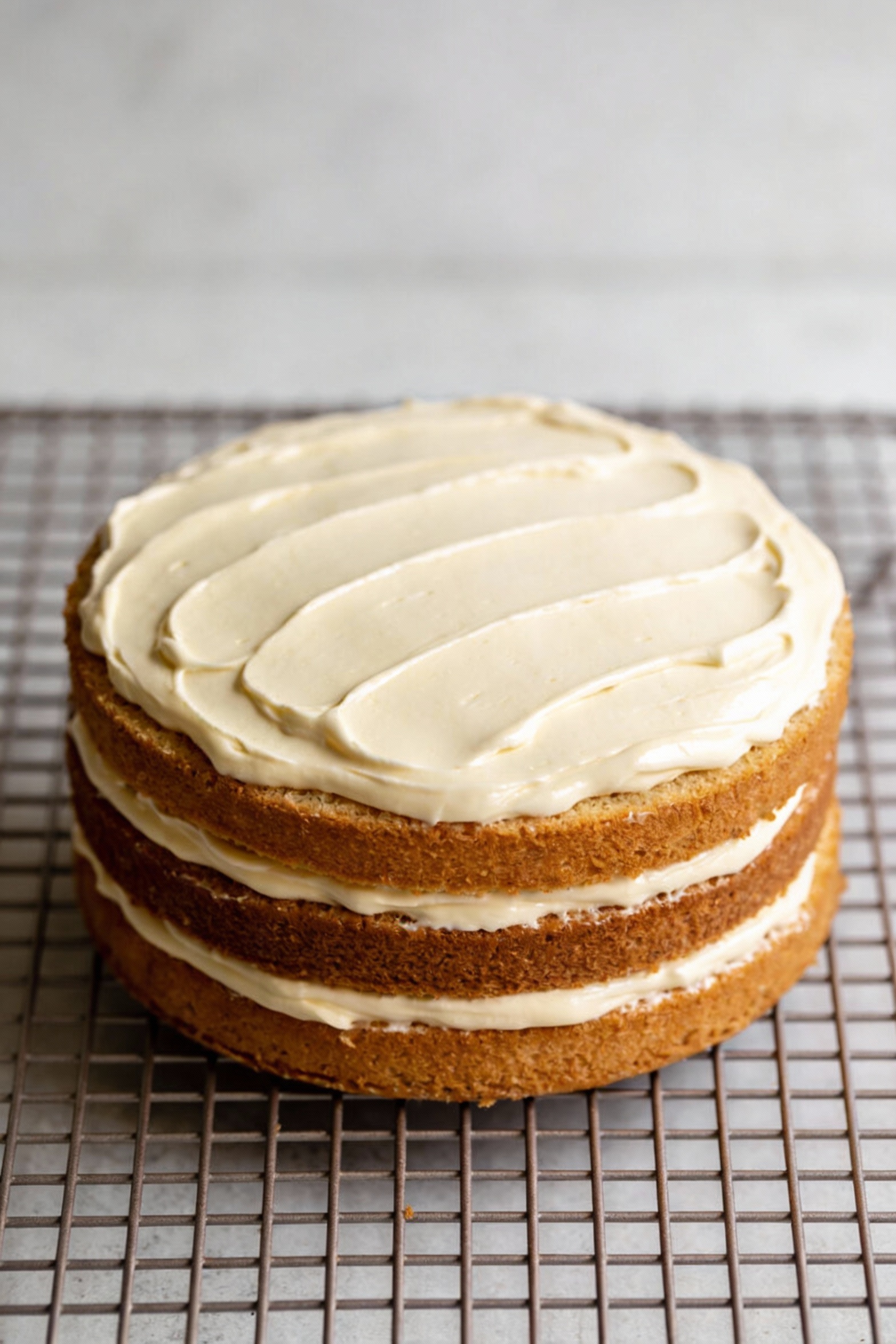 3. Cake layers cooling on a wire rack with a glossy vanilla buttercream being smoothly spread across the top (offset spa