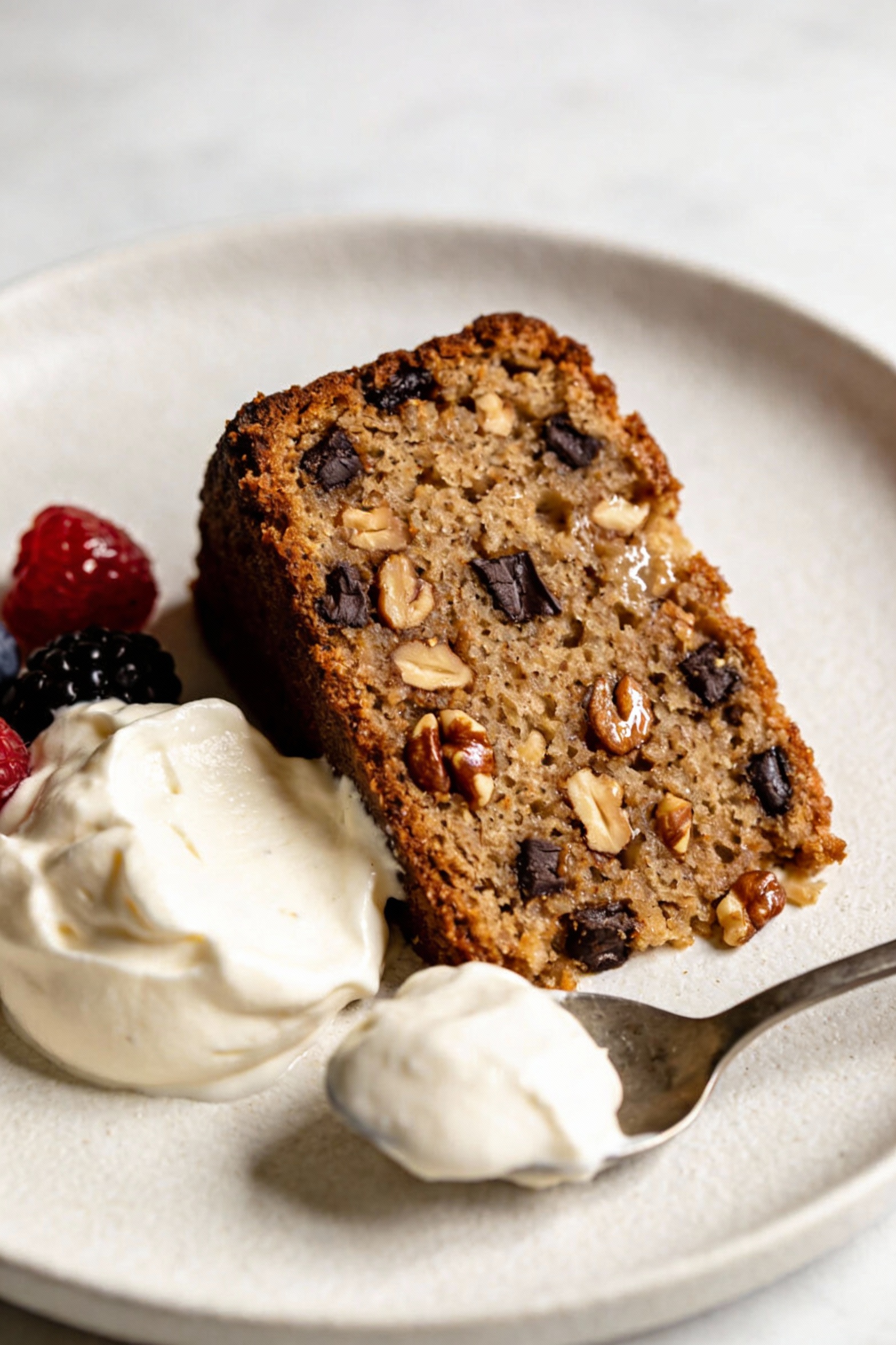 4. Final plated dish: a single slice of moist banana-yogurt cake on a matte white dessert plate, visible tender crumb wi