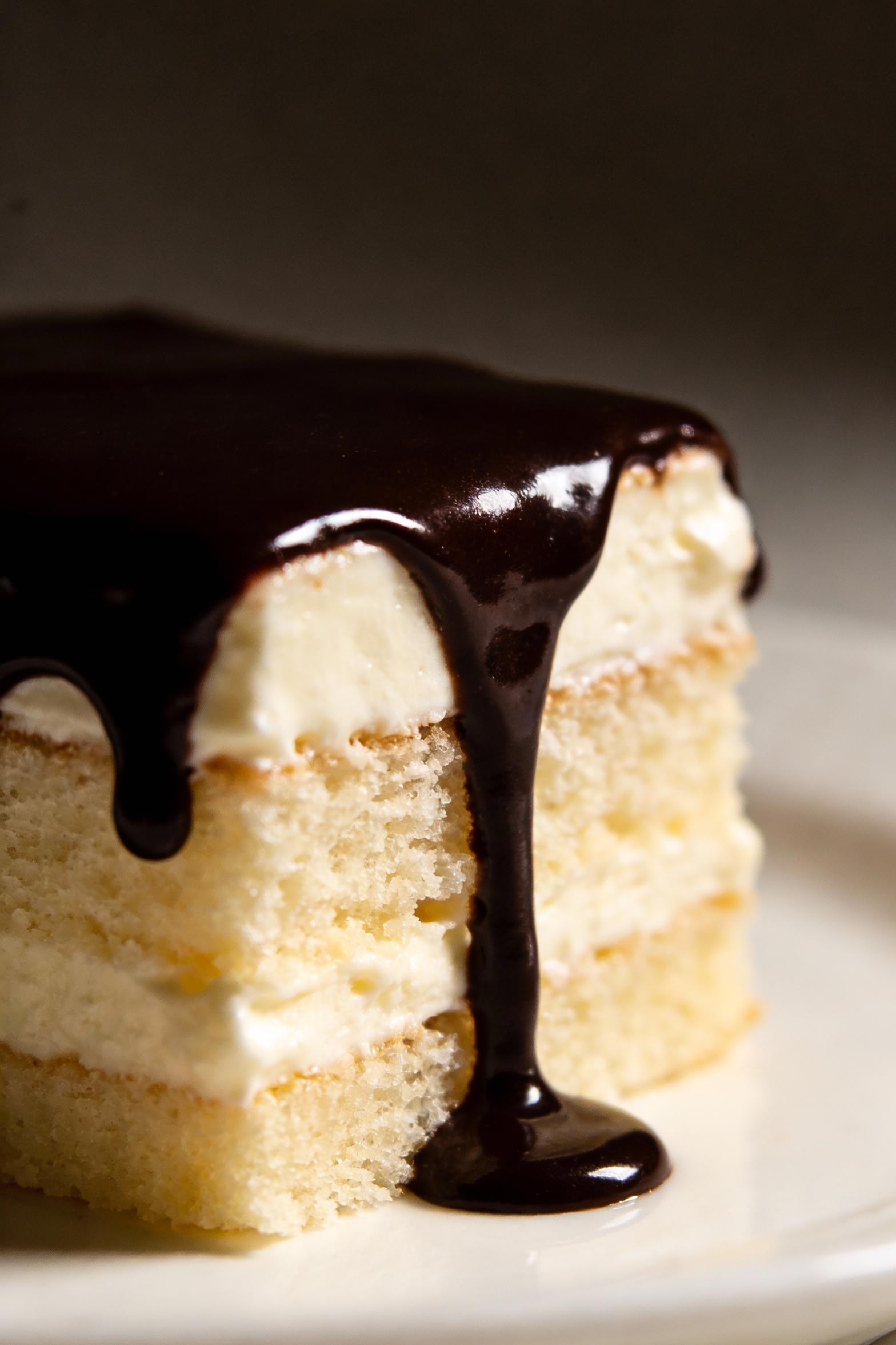 4. Close-up detail of chocolate ganache drips on a vanilla cake slice (ganache glossy and dark), contrast between rich f